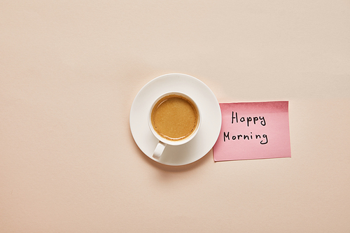 top view of coffee and sticky note with happy morning lettering on beige background