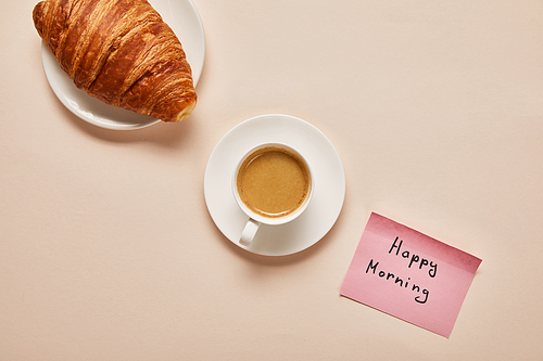 flat lay with coffee, croissant and sticky note with happy morning lettering on beige background