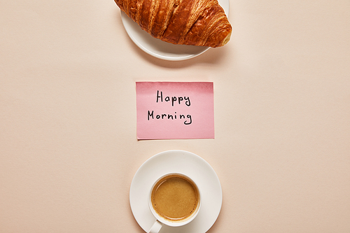 flat lay with coffee, croissant and sticky note with happy morning lettering on beige background