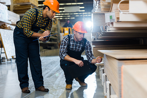 two multicultural colleagues in uniform and helmets working in warehouse