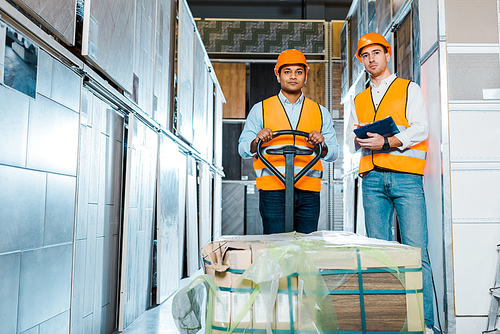 concentrated multicultural warehouse workers standing near pallet jack in warehouse