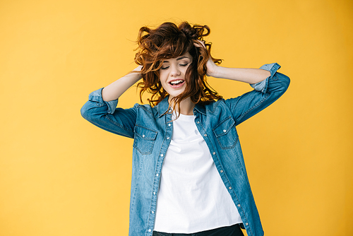 beautiful curly woman touching hair and smiling while standing on orange