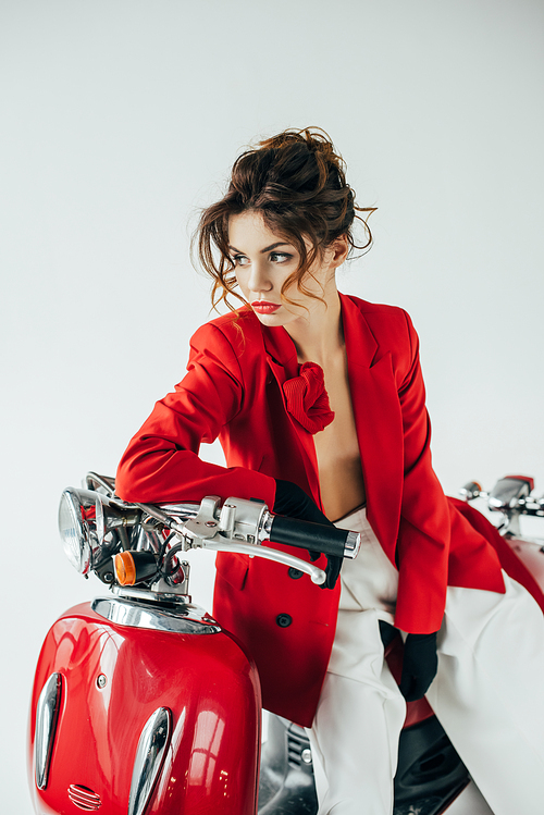 serious and stylish young woman sitting on red motorcycle on white