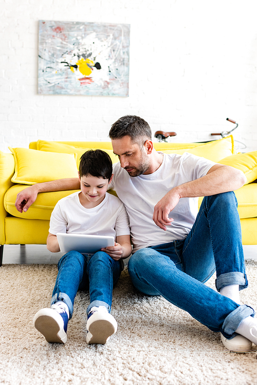 father and son sitting on carpet and using Digital Tablet in Living Room