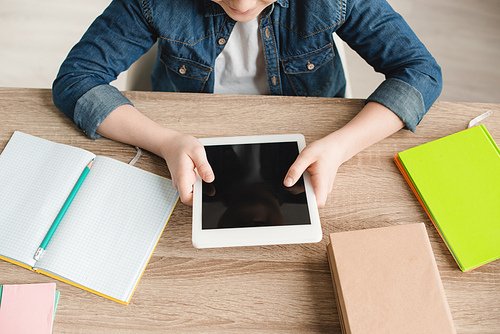cropped view of boy holding digital tablet with blank screen while sitting at desk with notebooks