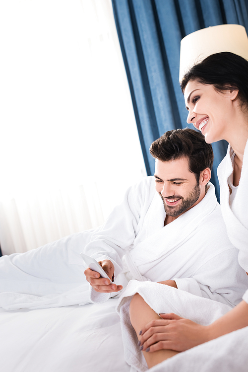 cheerful bearded man using smartphone near happy brunette woman