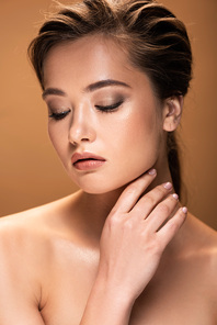 young naked woman with shiny makeup touching face isolated on beige
