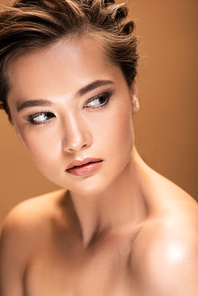 beautiful naked woman with shiny makeup looking away isolated on beige