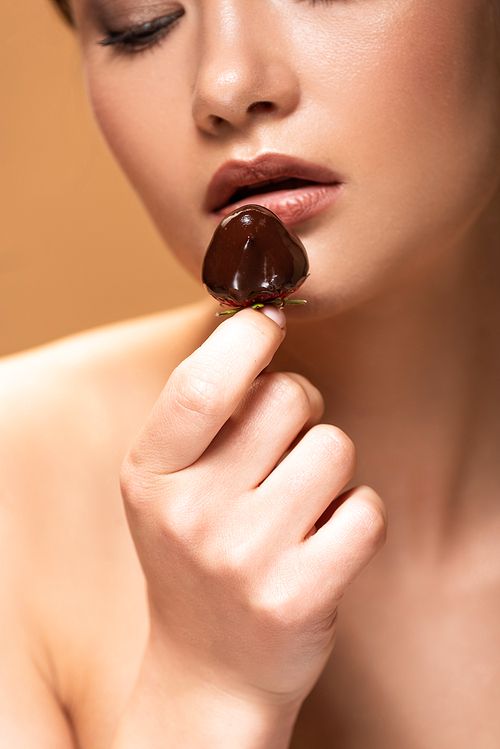 young naked woman looking at strawberry in melted chocolate isolated on beige