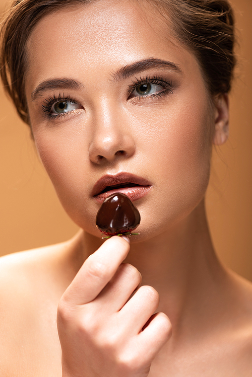 dreamy beautiful naked woman holding strawberry in melted chocolate isolated on beige
