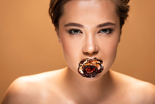 young naked woman holding rose in mouth covered with melted chocolate isolated on beige
