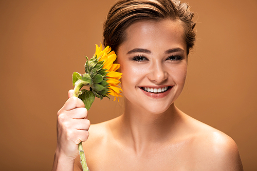 beautiful smiling naked woman with yellow sunflower isolated on brown