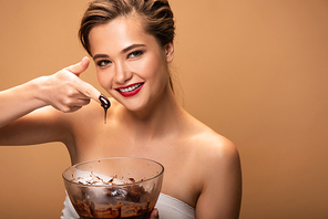 happy beautiful woman showing finger in melted chocolate isolated on beige