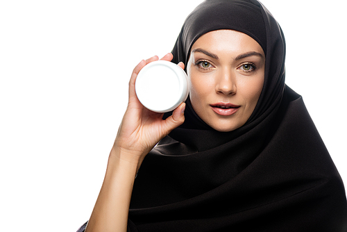 young Muslim woman in hijab holding container with cosmetic cream isolated on white
