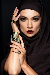 beautiful Muslim woman in hijab with makeup in golden rings and bracelet isolated on black