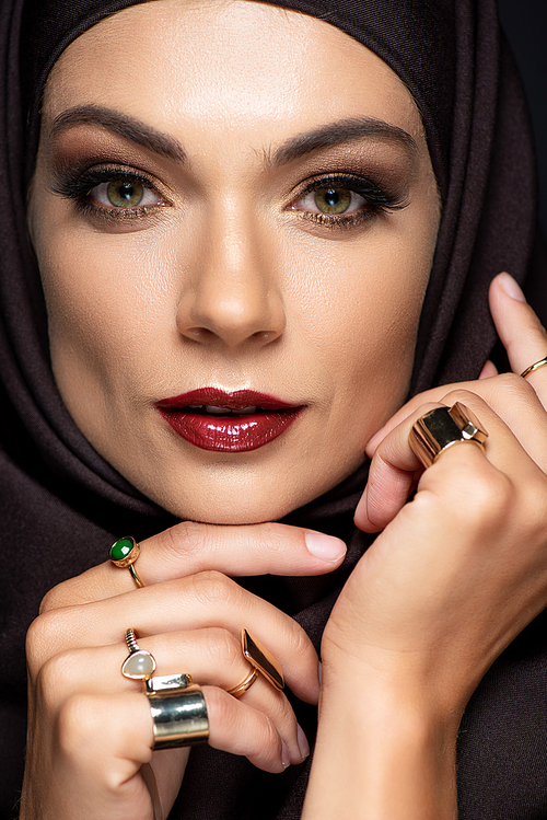 beautiful Muslim woman in hijab with makeup in golden rings isolated on black