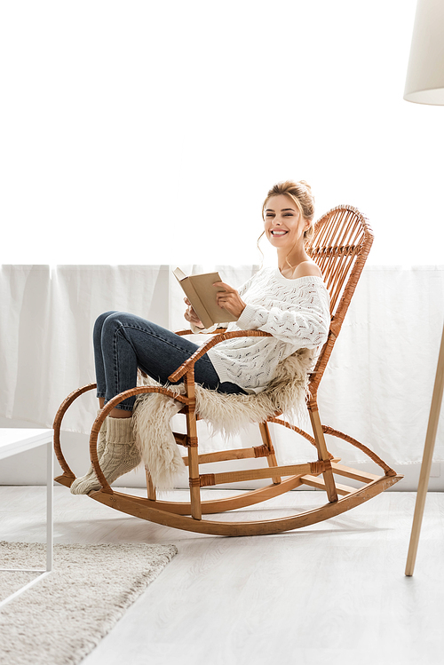 attractive woman in white sweater sitting on rocking chair and holding book