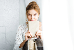 attractive woman in white sweater with blanket holding book