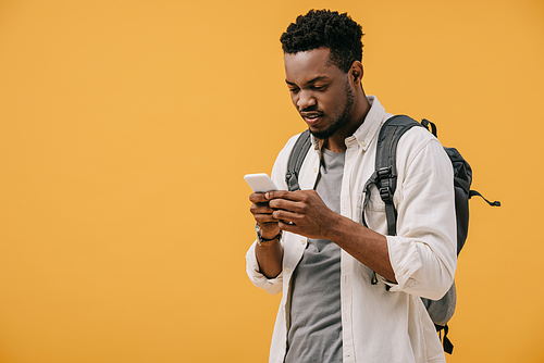 handsome african american man with backpack using smartphone isolated on orange