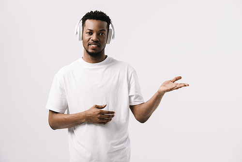 cheerful african american man listening music in headphones and gesturing isolated on white