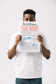 curly african american man covering face while holding newspaper with fake news lettering isolated on white