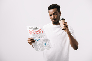 curly african american man holding paper cup and reading newspaper with fake news lettering isolated on white