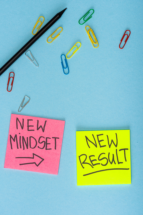 Top view of sticky notes with new mindset and new result lettering with paper clips and pencil on blue