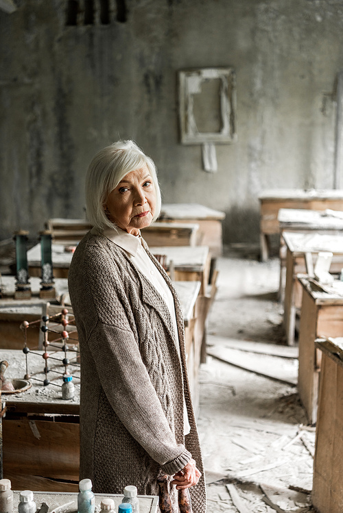 sad retired woman with grey hair standing in dirty classroom