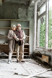 retired couple looking at window while standing in damaged classroom