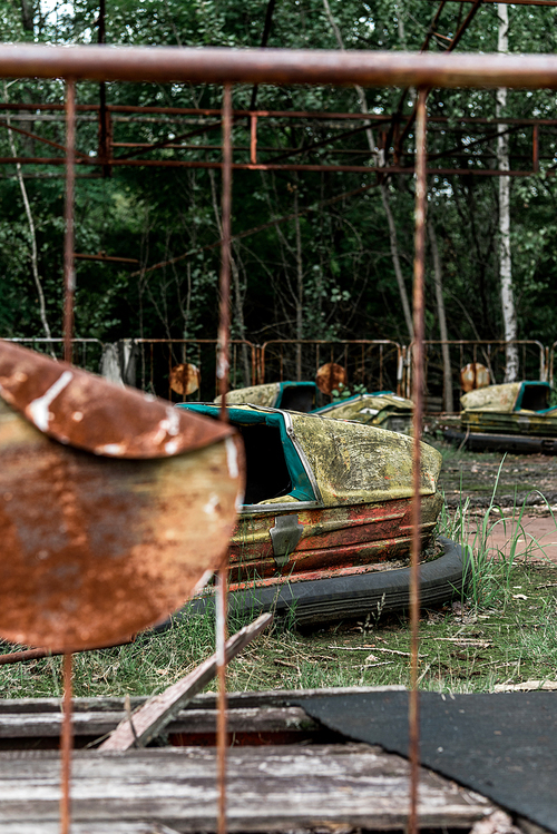 selective focus of abandoned bumper cars in amusement park near metallic fence