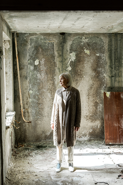 senior woman with grey hair standing in empty and dirty room