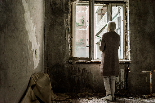 back view of retired woman holding plant in empty room near windows
