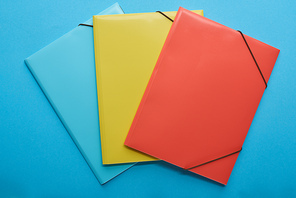 top view of red, blue and yellow paper binders isolated on blue
