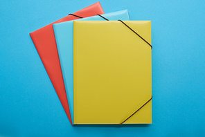top view of red, blue and yellow paper binders isolated on blue