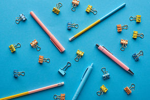 top view of pens, pencils and paper clips isolated on blue