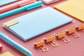 selective focus of notebook, paper clips and colorful stationery supplies on pink