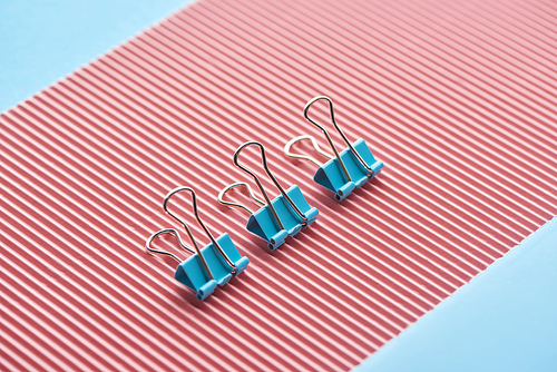 metal paper clips on textured pink paper isolated on blue