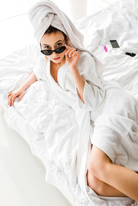 overhead view of stylish woman in bathrobe, jewelry, towel and sunglasses lying in bed and 