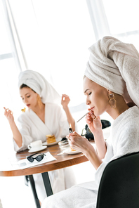 selective focus of stylish woman in bathrobe and jewelry with towel on head lighting up cigarette