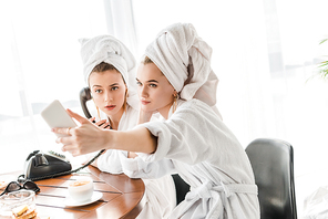 selective focus of stylish women in bathrobes and jewelry with towels on heads talking on retro phone and taking selfie