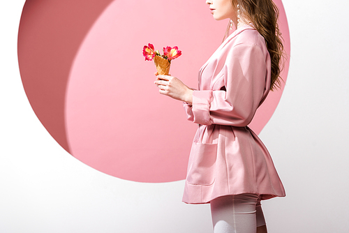 cropped view of woman holding ice cream cone with flowers on white and pink
