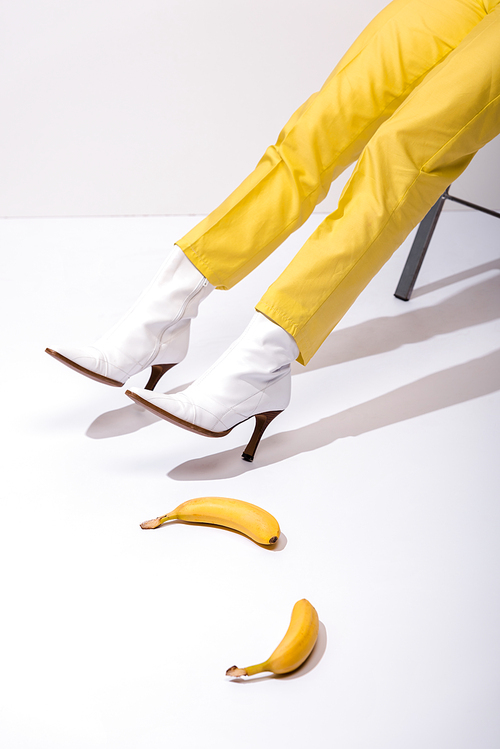 cropped view of woman in boots near bananas on white