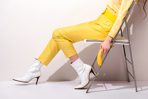 cropped view of woman sitting on chair and holding yellow banana on white