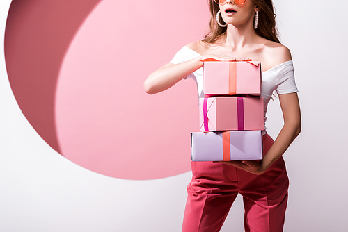cropped view of surprised woman holding presents on pink and white