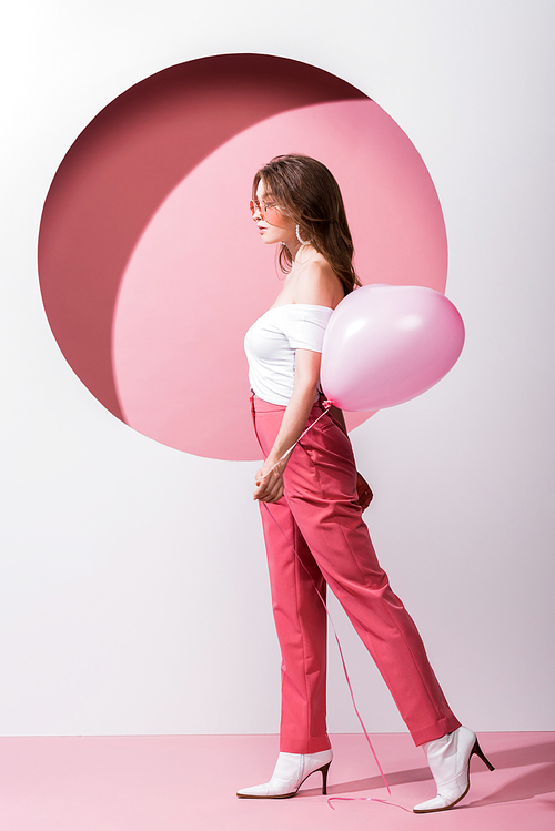 side view of attractive woman holding balloon on pink and white