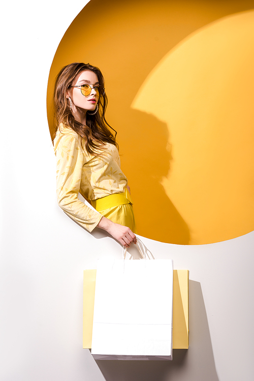 young attractive woman in sunglasses holding shopping bags on orange and white
