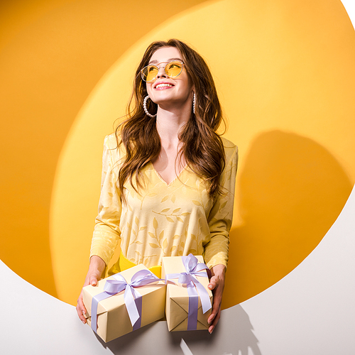 happy woman in sunglasses holding gifts on orange and white
