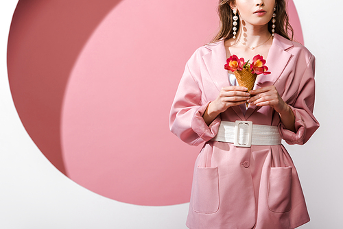 cropped view of woman holding ice cream cone with flowers on pink and white