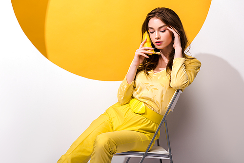 young woman sitting on chair and holding banana on white and orange