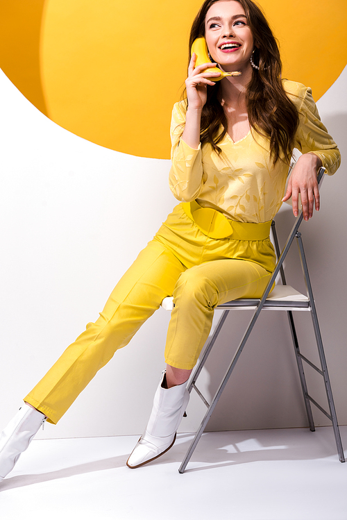 happy young woman sitting on chair and holding banana on white and orange